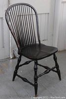 Front angled view of antique bow back spindle chair showing the bow back, vertical spindles, sculpted seat, and turned legs with stretchers.