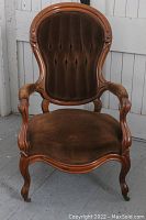Antique brown velvet gentleman's parlour chair with carved wooden frame and cabriole legs on casters, shown from front view.