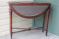 Front view of the antique folding card table showing the semi-circular tabletop with leather inset and four turned legs.
