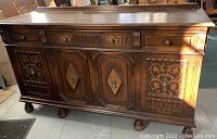 Front view of carved oak buffet sideboard showing top surface, two drawers, and four cabinet doors with ornate carvings, raised on bun feet.