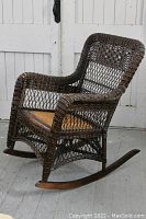 Side-angle view of the antique Victorian wicker rocking chair showing woven wicker pattern, cane seat, and curved wooden rockers on a gray wooden floor.
