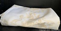 Folded view of the cream-colored fabric with subtle golden damask pattern visible.