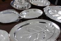 Main view of the vintage silver-plated serving trays and dishes arranged on a wooden surface, showing various shapes and embossed details.