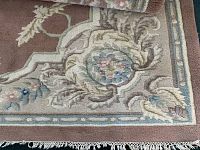 Close-up of carpet corner showing detailed floral and ornamental designs in pink, blue, cream, and green shades with fringed edge