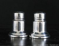 Pair of small silver salt and pepper shakers shown front-facing on a black surface.