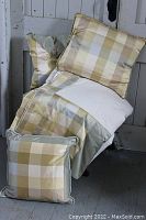 Photo of a queen sized checked silk and wool blend blanket draped on a chair, accompanied by two matching checked cushions with light blue/grey trim and fabric rosette detail.