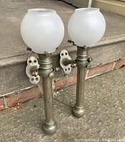 Pair of vintage articulating ship's sconce lights with frosted white glass globe shades resting on concrete steps in daylight.