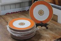 Stack of seven charger plates with protective tissue between each and one plate displayed on decorative stand