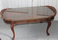 Full view of vintage carved wood coffee table with glass top, showing ornate carved details at edges and shape of legs.