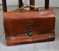 Front view of vintage brown calf leather Bugatti briefcase showing embossed brand name, flap with key lock closure, and handle.