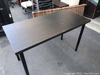 Photo of one black rectangular desk with metal legs taken outdoors on concrete