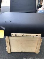 Front view of black padded adjustable massage table surface with wooden base and EarthLite branding, showing wear on upholstery.