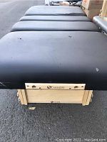 Top-down view of black padded massage table with Earthlite logo on the side, showing wear on surface and edge.