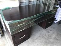 Front and side view of the brown office desk showing desktop surface, drawer handles and plastic wrapping