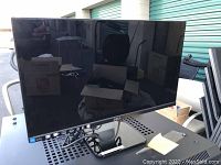 Image shows one Dell widescreen computer monitor with black bezel and stand. The screen is blank and reflective showing a storage unit background.