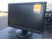 Photo of black Hanns G flat screen computer monitor with a round base stand and sticker on upper right corner of screen.