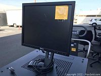 Photo of a Dell black bezel computer monitor with adjustable stand and power cable coiled at the base, outdoors setting.