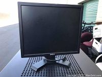 Single Dell computer monitor shown from front angled view on a perforated metal surface with surrounding storage items.