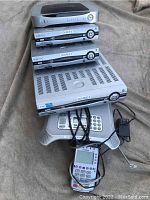 Photo of four Channel Vision DVR units labeled Source 1 to Source 4 stacked together with a Motorola cordless phone handset, base, a remote, and AC adapter on a beige surface.