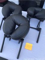 Three black leather padded headrest cushions with U-shape design mounted on adjustable black metal frames.
