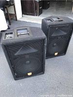 Two JBL speakers angled on concrete floor