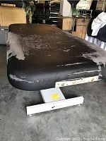 Full length top view of the massage table showing worn and torn black upholstery surface with Earthlite brand plate on metal base.