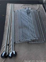 Photo showing 5 metal wire shelves, 4 metal poles, and 3 caster wheels laid out on a fabric surface
