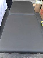 Top view of black cushioned massage table surface showing two sections and face cradle holes.