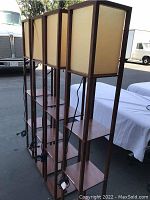 Photo of 4 spa floor lamps with wooden frames, shelves, and light diffuser shades standing outdoors.