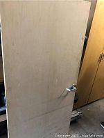 Unpainted solid wood door with visible metal lever handle, standing upright showing front surface.