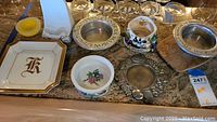 Assorted plates, bowls, decorative metal items, and ceramic cutting board on counter