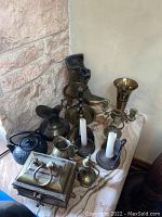 Image showing assortment of brass and metal decorative items arranged on a marble surface by a stone wall.