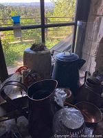 Photo showing a group of metal and ceramic decor pieces on a surface near a window, includes copper and brass vases, blue enamel pot, and ceramic planter.