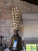 Photo showing hammered copper vase holding dried floral arrangement with beige buds and twigs against a stone wall.