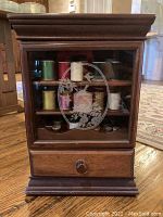 Front view of vintage wooden curio cabinet with etched glass door showing sewing thread spools inside