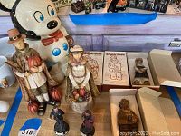 Wide view showing large Mickey Mouse cookie jar, Tremar Pottery pilgrim figurines, boxed Figurines collectibles, and small standing and seated figures arranged on wooden surface.