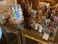 Full view of Fitz and Floyd 'Ladies Dancing' ceramic figurine with assorted glass candle holders around it on a glass display cabinet.