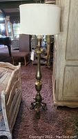 Full view of tall brass floor lamp with white drum shade showing overall design and height.