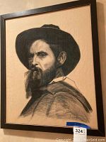 Framed portrait drawing of a man with beard and hat, photographed straight on showing the entire framed artwork