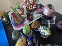 Glass decorative eggs with floral designs, iridescent paperweight, and salt and pepper shakers on white wood tray with green leaf border.