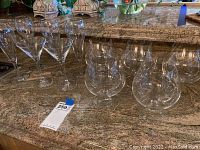 Set of twelve clear glass brandy snifter glasses arranged on a granite countertop, showing shape and size.