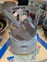 Front view of white Cuisinart ice cream maker with clear paddle inside and instruction booklet in background.