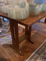 Wooden folding side table shown with glass and clear plastic dishes on top, highlighting table's wood grain and structure.