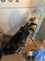 Full view of black Titleist golf bag standing with golf clubs and S2 headcovers in a basement room