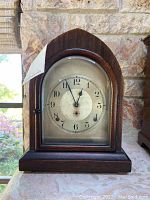 Front view of the vintage mantle clock showing the arched wooden case and clock face with Arabic numerals.