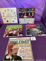 Five vintage Christmas record albums in their covers displayed on a purple cloth; covers include The Great Songs of Christmas, Christmas Sing-Along with Mitch, Nat King Cole, Christmas Around the World, Holiday Sing Along with Mitch