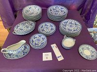 Overview of the lot showing multiple stacks of plates of different sizes, covered oval serving dishes, gravy boat, sugar bowl, and smaller side plates all decorated in blue and white floral and bird patterns.