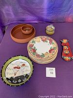 Lot items on purple cloth backdrop including plates, pasta bowls, ceramic jar, chip and dip bowl, decorative cat, and large chef plate.