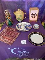 Full lot showing decorative plates, teacup and saucer, medicine cooker, lantern, fabric pieces, and a figurine