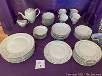 Full display of the dinnerware set showing plates, cups, creamer, and coffee pot arranged on a purple cloth.